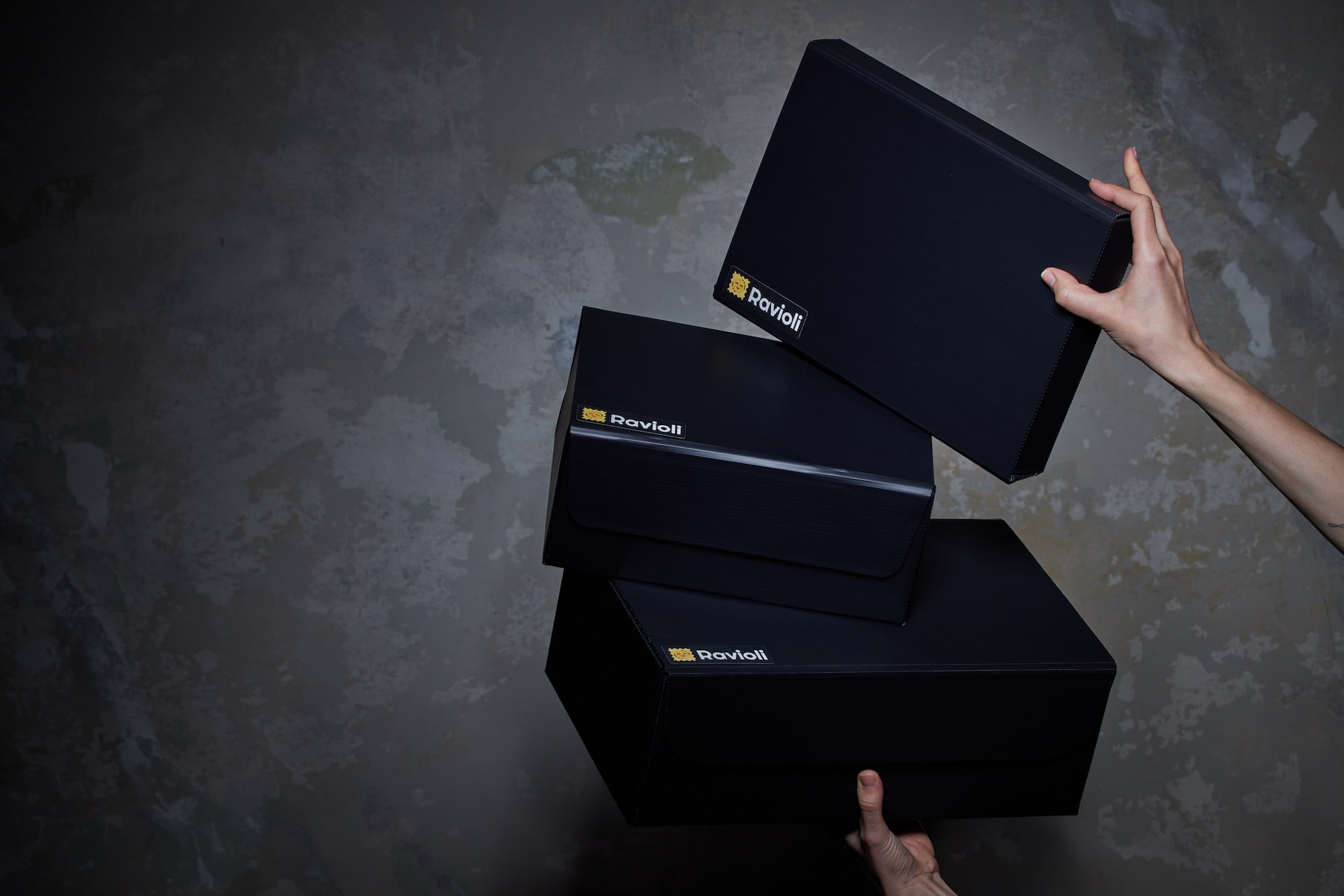Zwei Hände halten 3 Mehrweg-Versandverpackungen von Ravioli die aufeinander gereiht sind